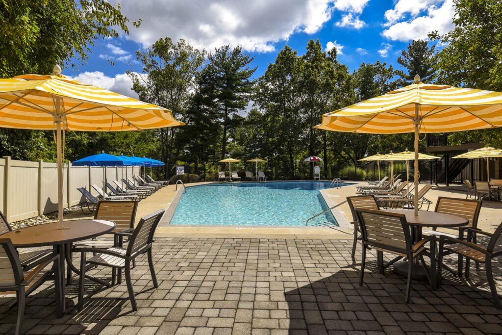 Radnor Crossing Pool in front of a line of green trees and umbrellas with tables and chairs.