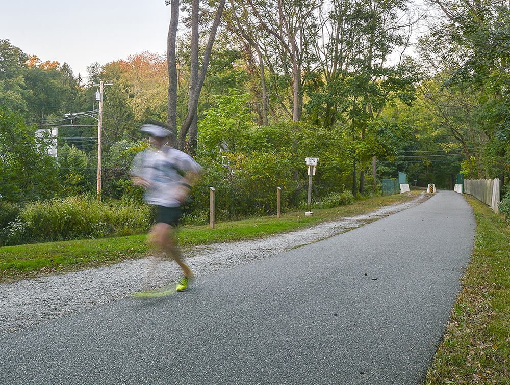 Person running on the wooded Radnor Trail with a paved path