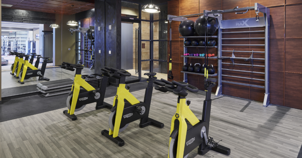 Fitness center with yellow spin bikes, weights, and medicine balls. 