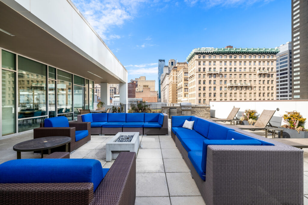 Firepit with several large outdoor couches on the roof of The Collins overlooking Philadelphia